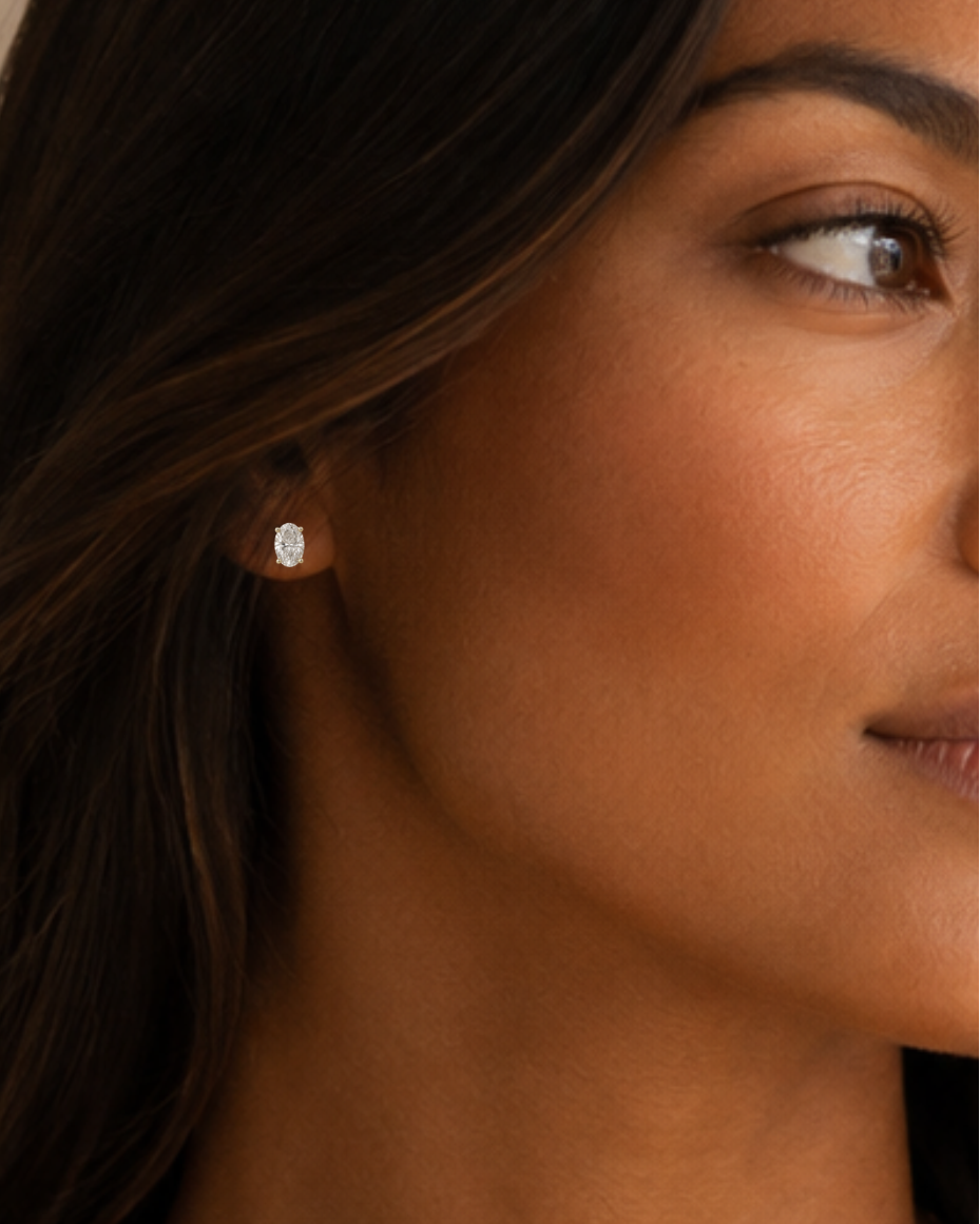 Woman wearing oval moissanite solitaire stud earrings in yellow gold